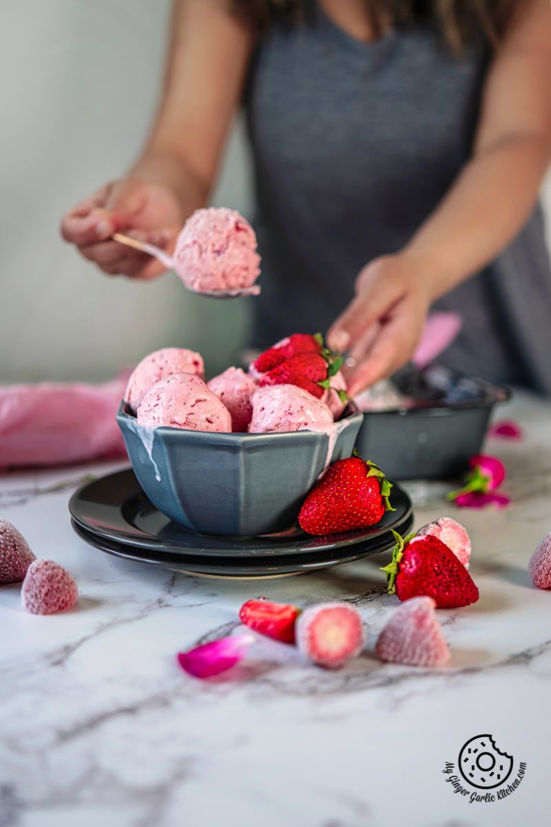 strawberry ice cream in a grey bowl and a female holding a spoon with strawberry ice cream in the background
