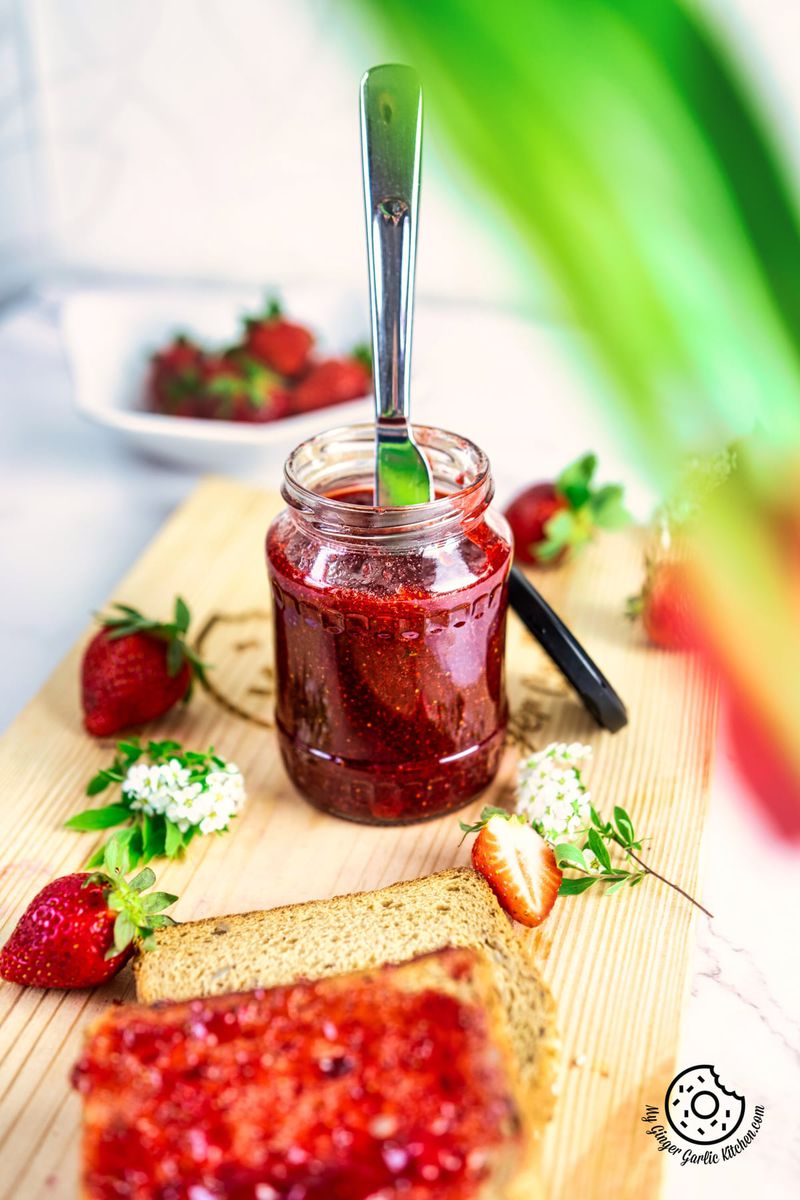 jar of strawberry jam with a knife in it and some strawberries on the side