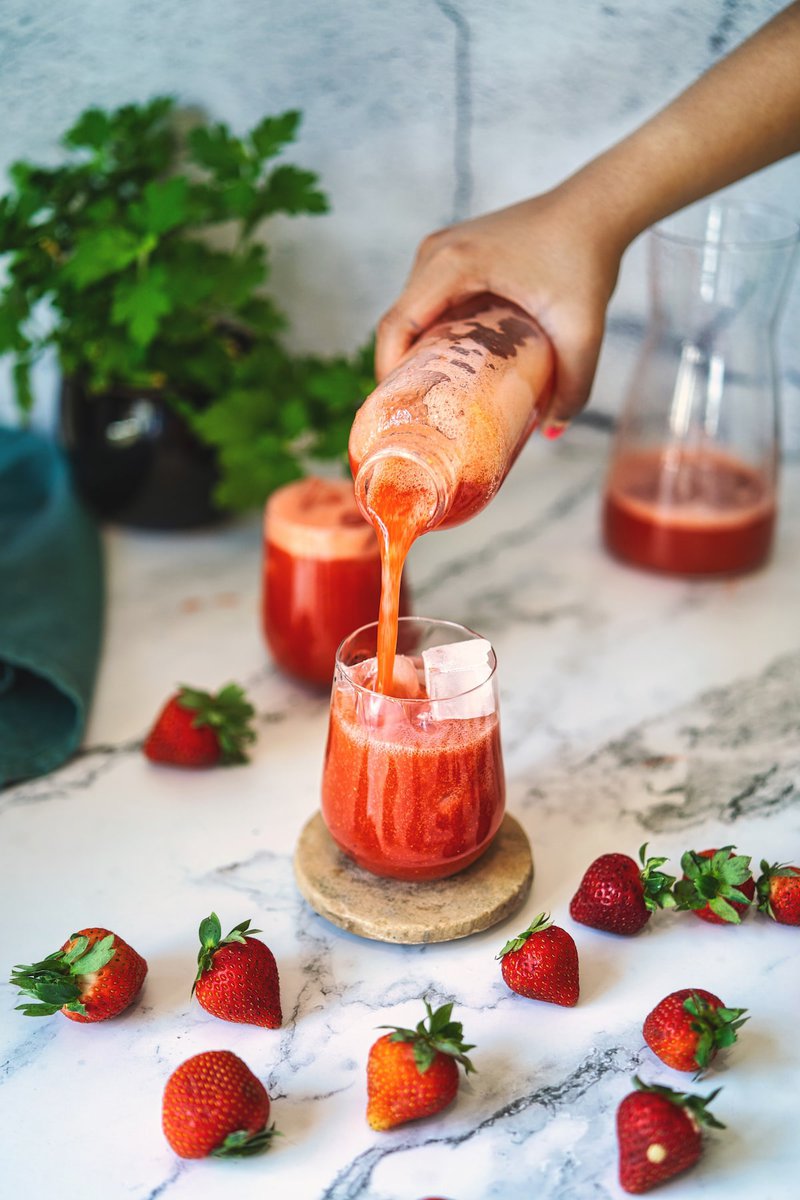 Pouring fresh homemade strawberry juice into a glass surrounded by whole strawberries.