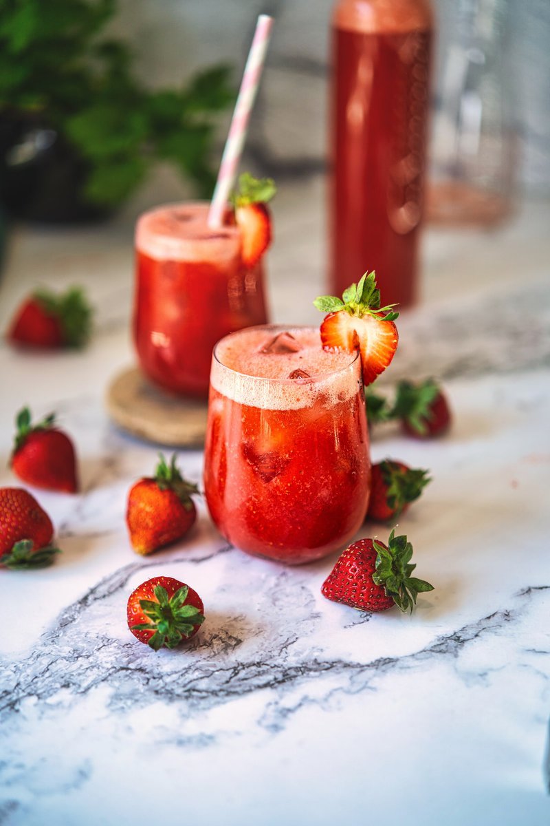 Two glasses of vibrant strawberry juice garnished with fresh strawberry slices.