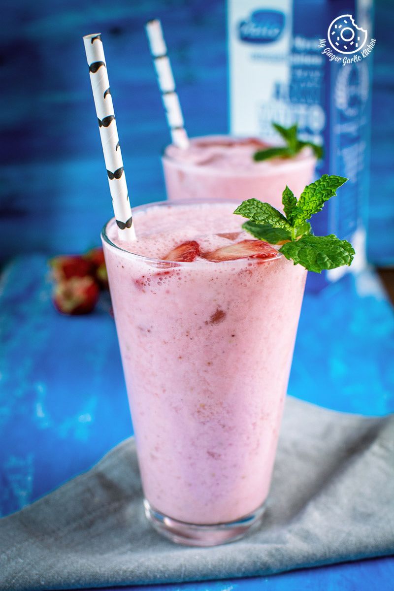 two glasses of strawberry lassi with strawberries and mint leaves