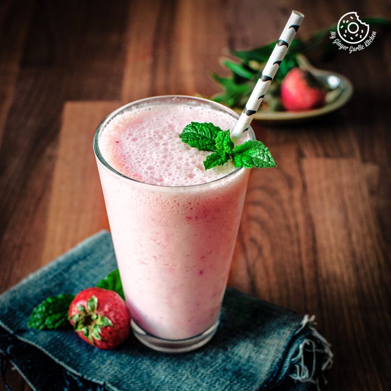 a glass of a strawberry lassi with a straw and mint