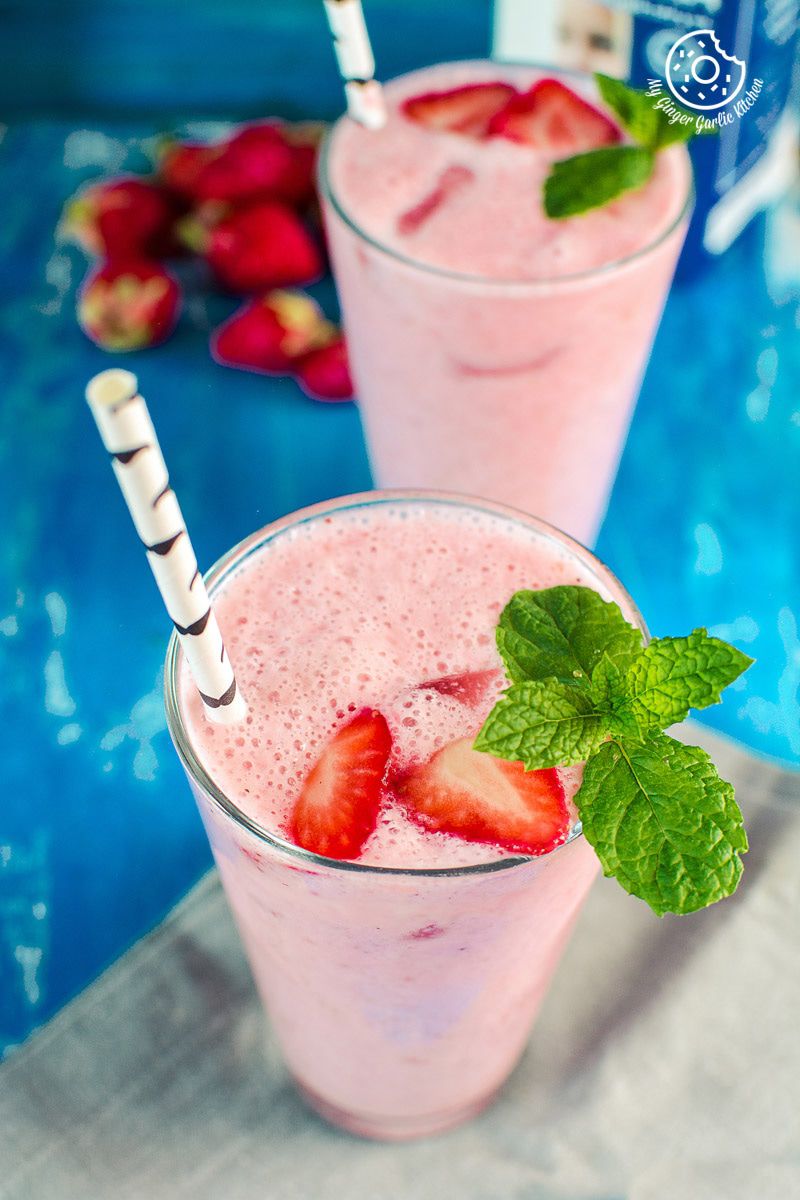 two glasses of strawberry lassi with strawberries on a blue table