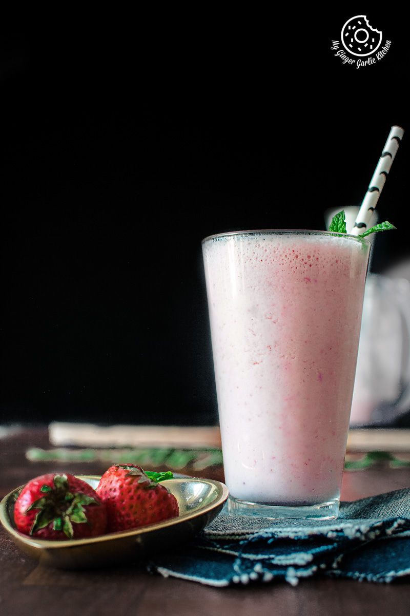a glass of strawberry lassi with strawberries on a table