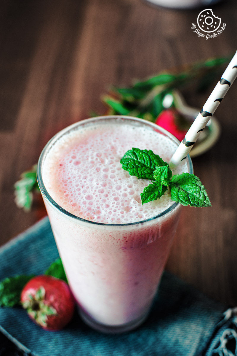 a glass of a strawberry lassi with a straw and mint