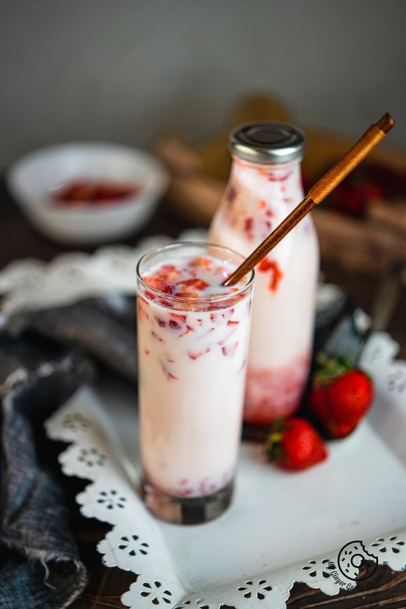 korean strawberry milk in a tall glass with a wooden spoon and a glass bottle