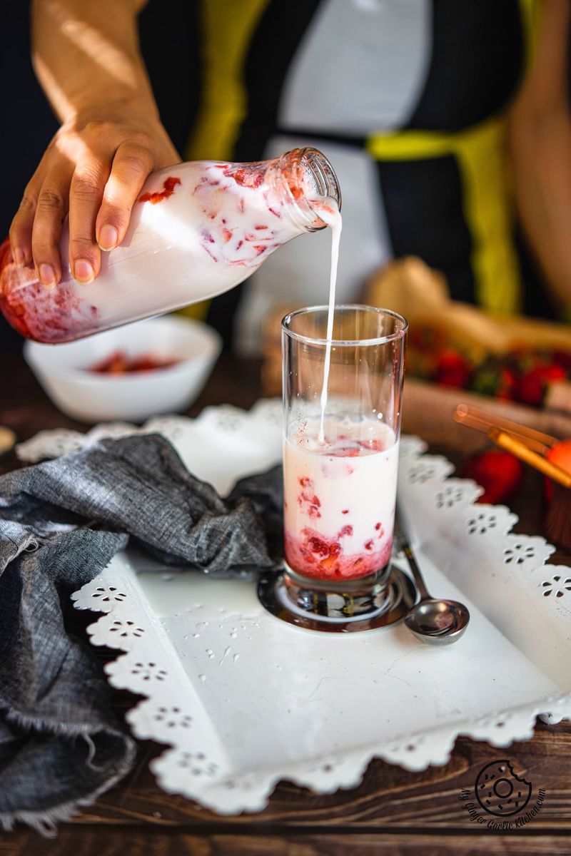 a female pouring strawberry milk from a glass bottle into a tall glass