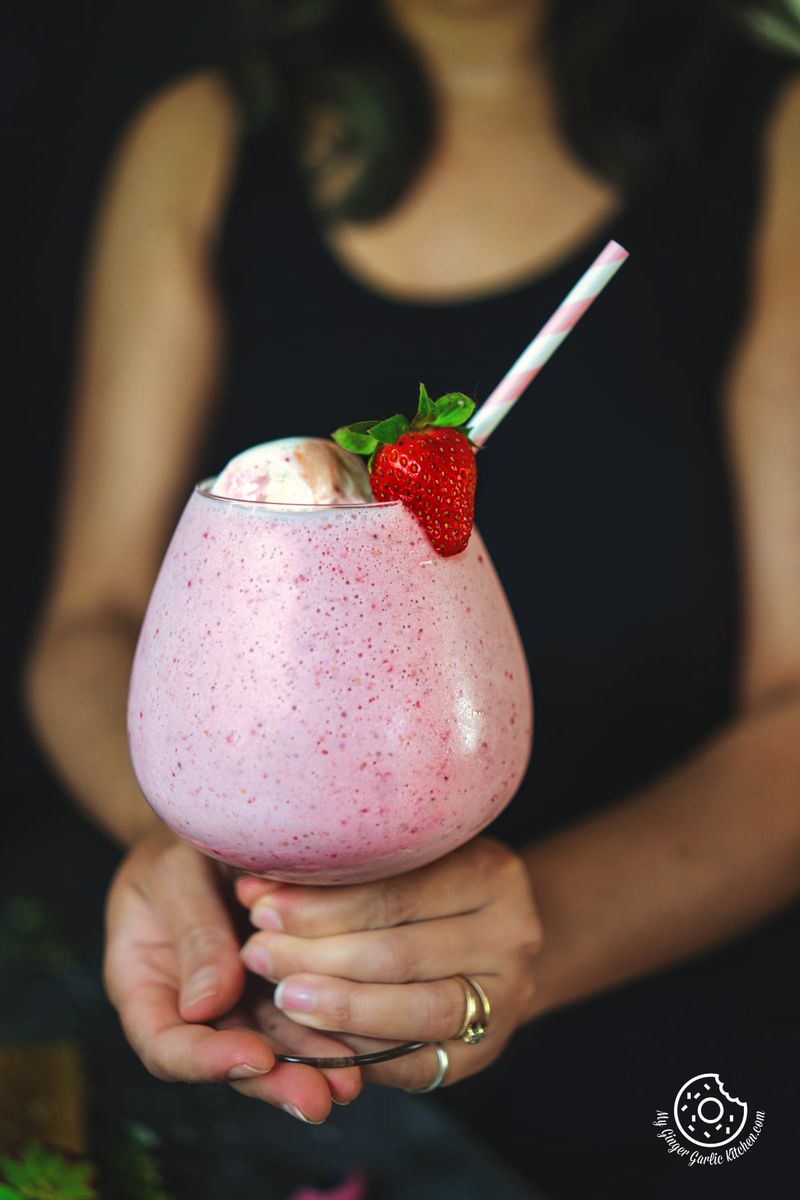 a female holding a strawberry milkshake glass topped with ice cream and strawberry