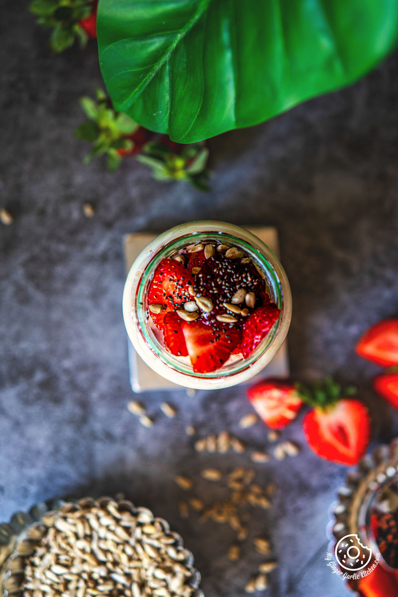Top view of a jar of creamy strawberry overnight oats topped with strawberry slices and chia seeds with some sliced strawberries on the side