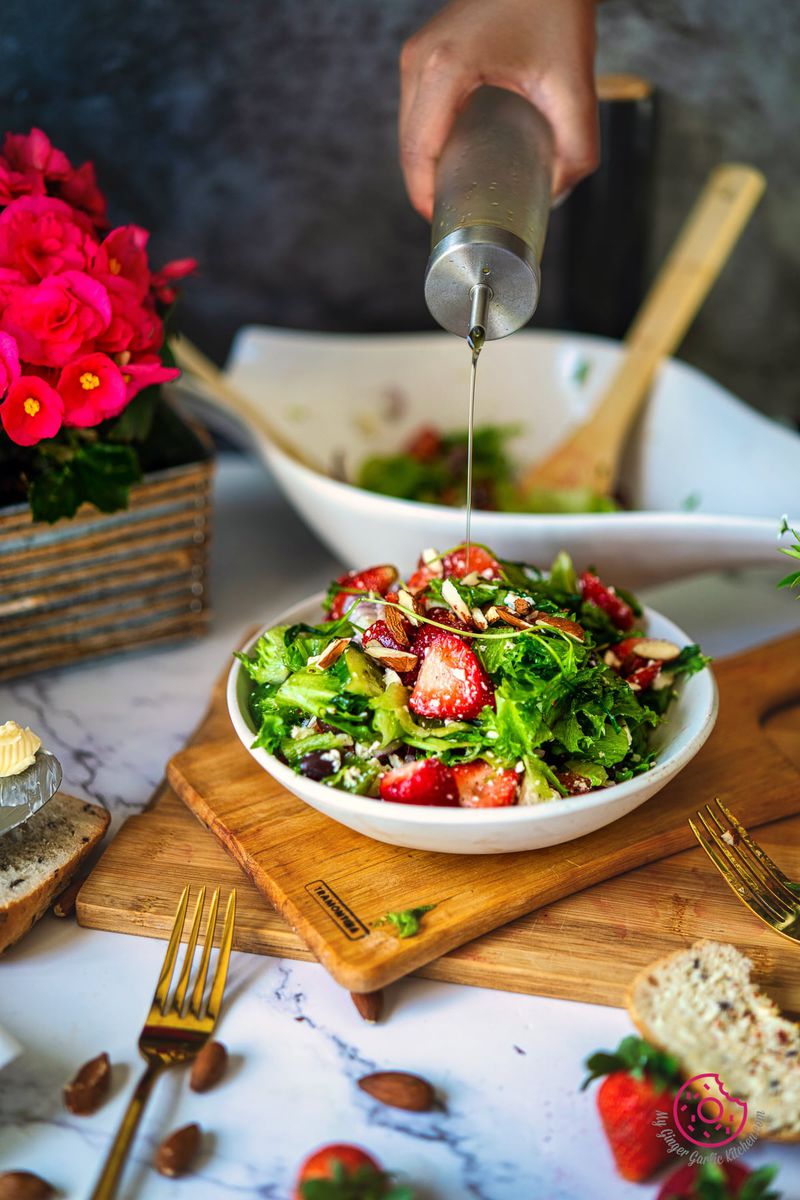 a hand drizzling olive oil over strawberry salad bowl