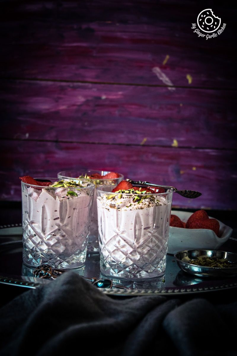 two glasses of strawberry shrikhand on a tray with a spoon