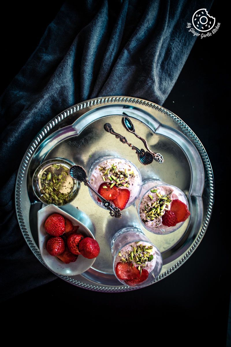 strawberry shrikhand in glassses with strawberries and pistas in bowls on a silver tray