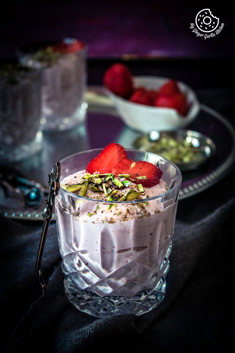 a glass of strawberry shrikhand topped with strawberries and pistachios