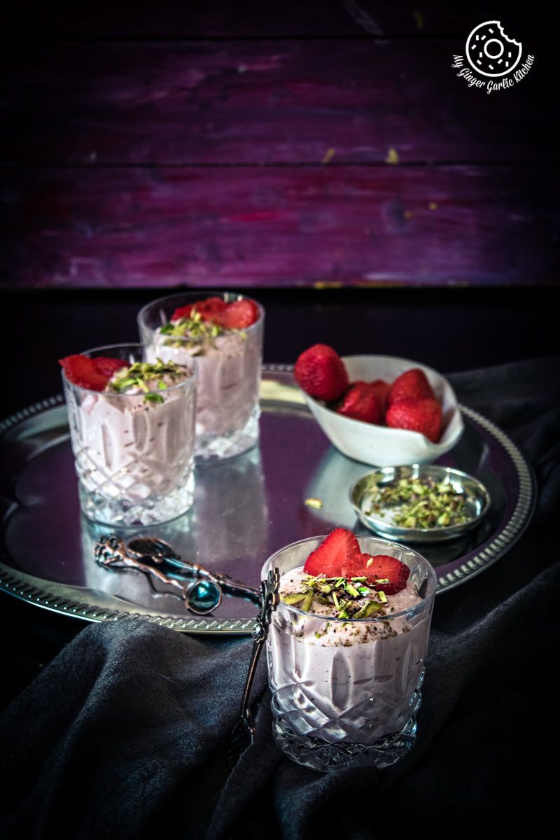 two glasses of strawberry shrikhand with strawberries on a tray