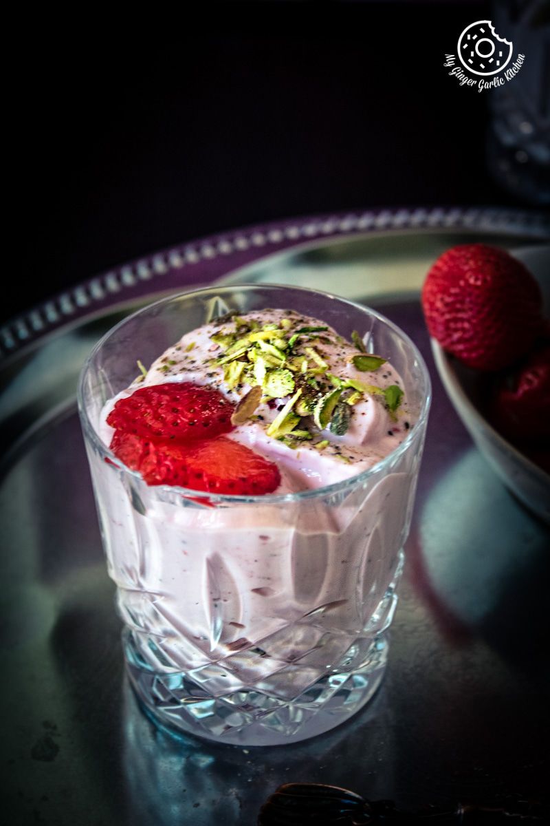 a glass of strawberry shrikhand with sliced strawberries and a bowl of strawberries