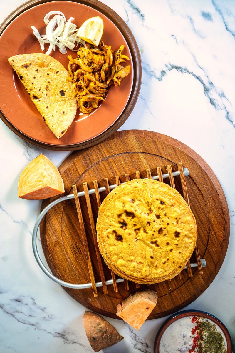 Golden sweet potato flatbread served with onions, lemon, and a side of sautéed vegetables on a brown plate.