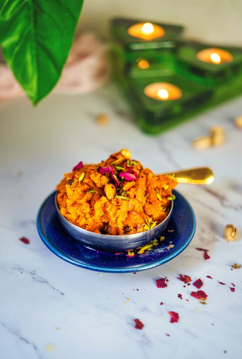 Homemade sweet potato halwa garnished with pistachios and rose petals served in traditional silver bowl for Diwali celebration