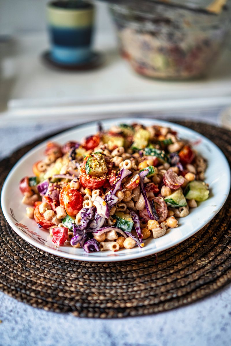 A vibrant tahini pasta salad with cherry tomatoes, cucumbers, red cabbage, and chickpeas on a white plate.