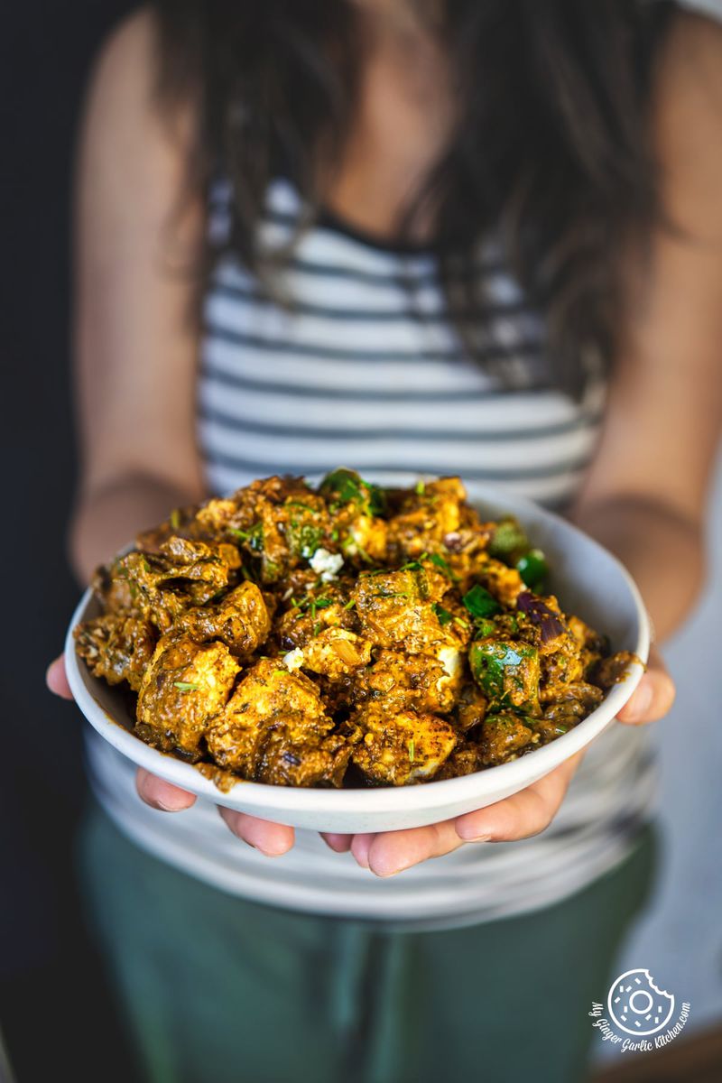 photo of a woman holding a bowl of tawa paneer with a spoon