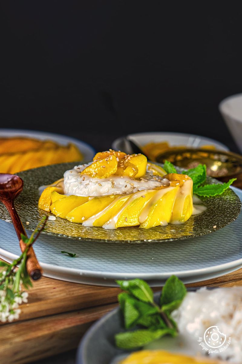 closeup shot of thai sticky mango rice topped with toasted sesame seeds and garnished with a mint sprig