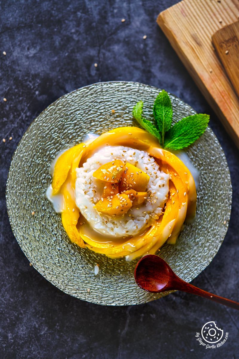 overhead closeup shot of thai mango sticky rice topped with toasted sesame seeds and garnished with a mint sprig