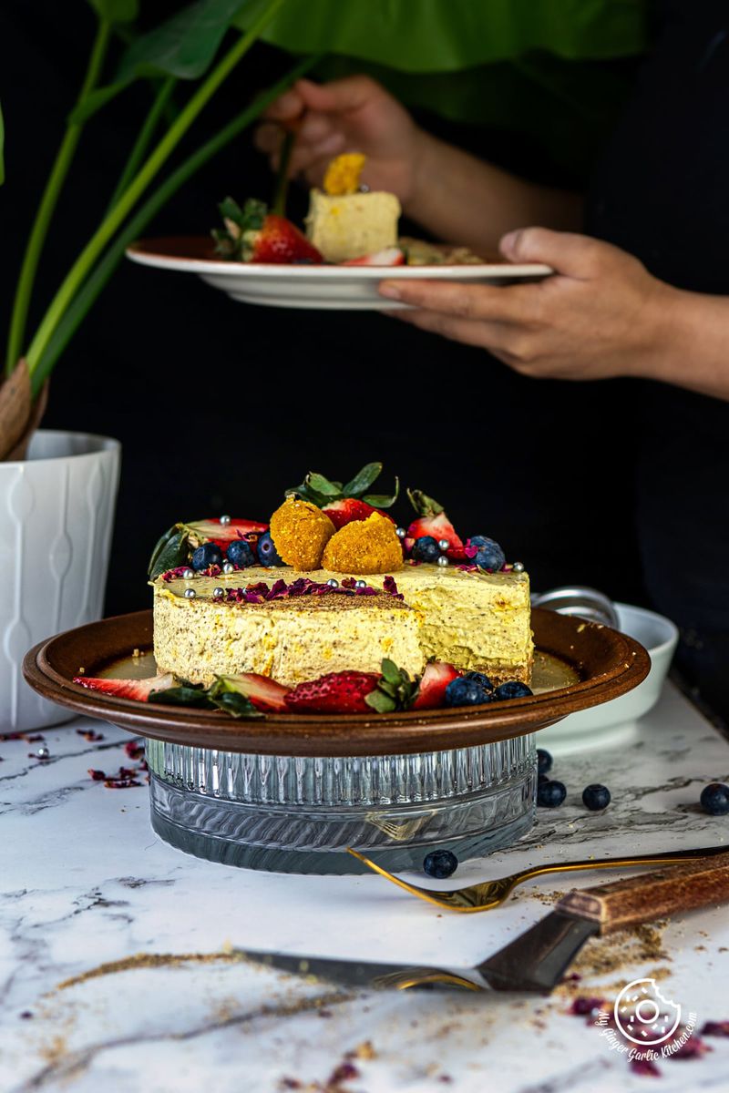 Thandai Cheesecake on a brown plate and a female holding a plate with cheesecake slice