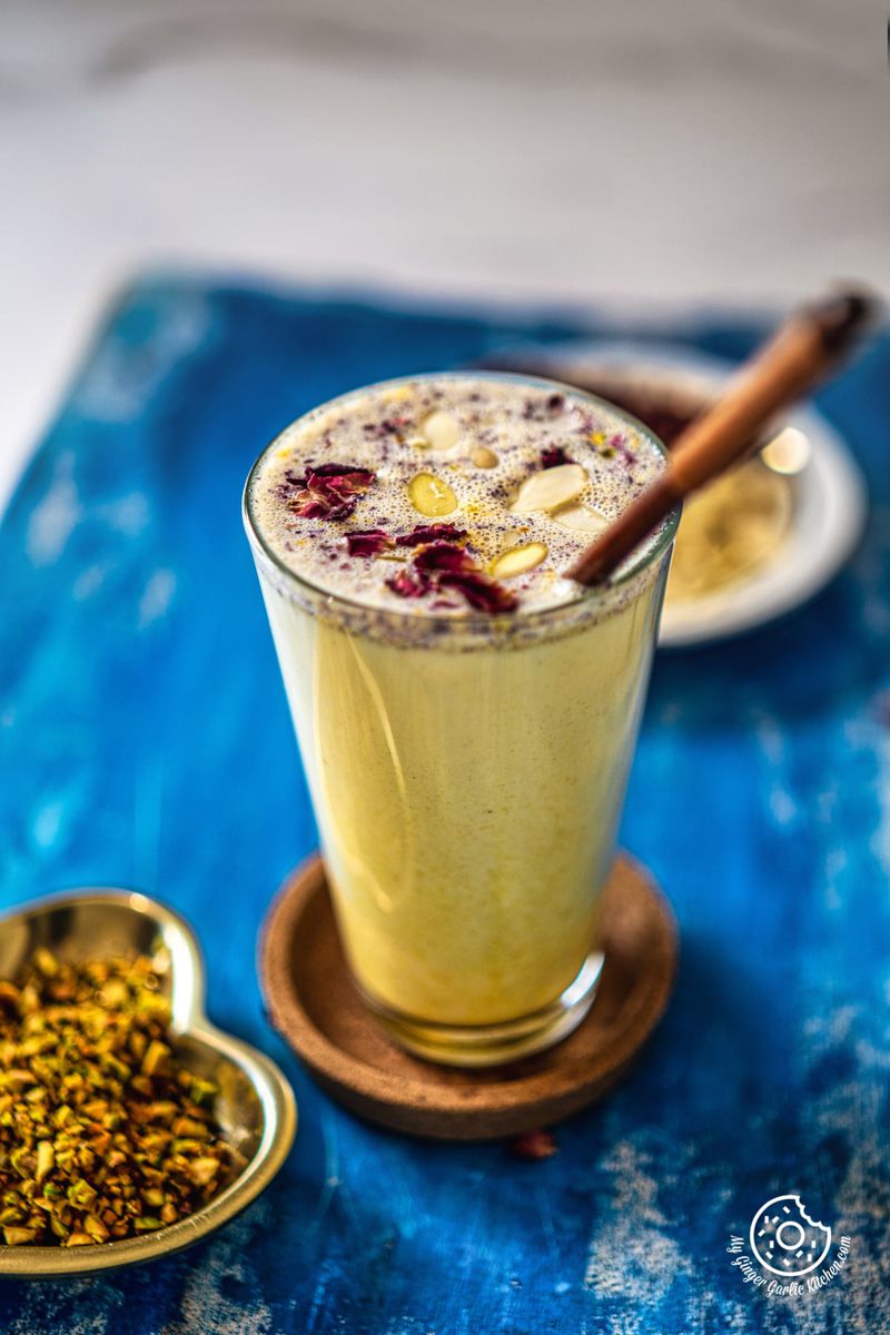 thandai milkshake topped with dried rose petals in a transparent glass kept on a wooden coaster
