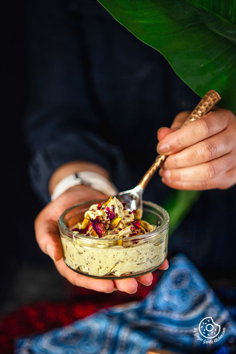 a female holding transparent bowl of thandai shrikhand