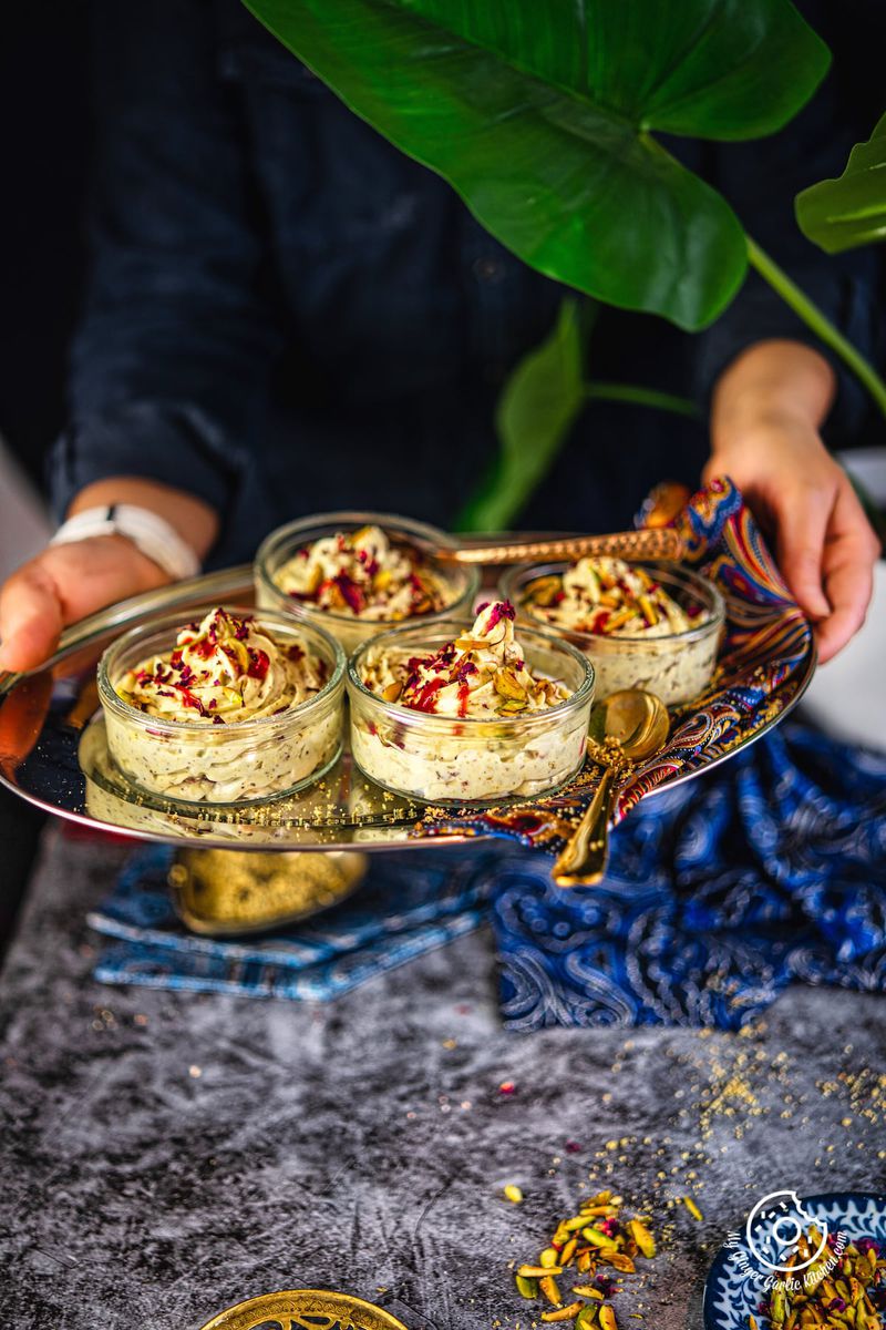 a female holding a metal tray with 4 transparent thandai shrikhand bowls