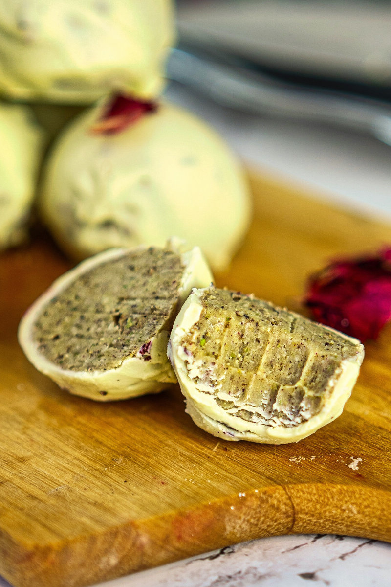 Thandai truffle cut in half on a wooden board showing a rich, spiced filling, with whole truffles and rose petals in the background.