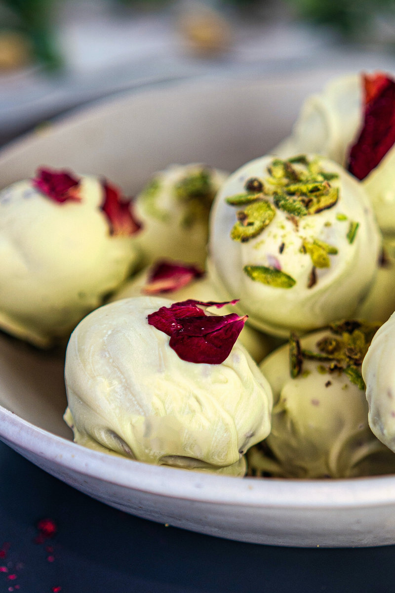 Close-up of white chocolate Thandai truffles topped with crushed pistachios and dried rose petals on a ceramic plate.