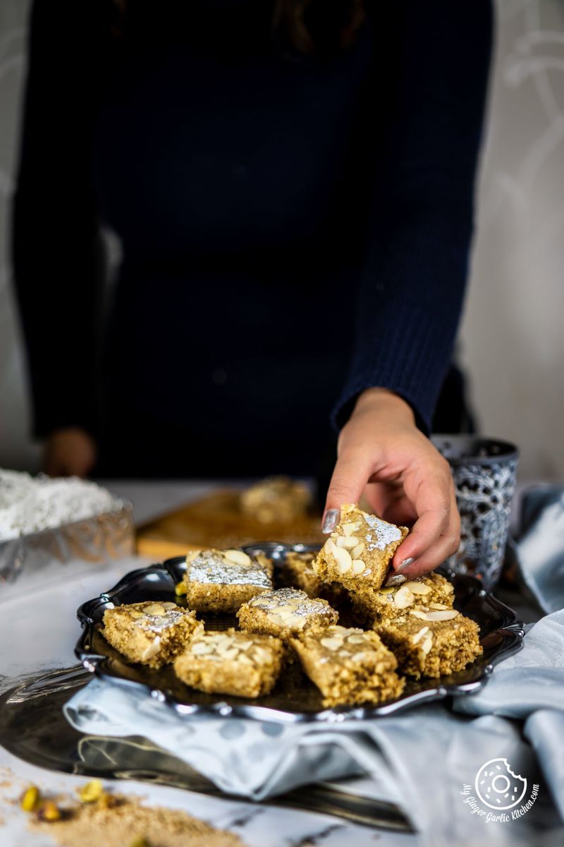 a hand holding til burfi piece served in a metal plate