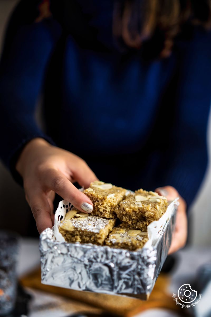 a female holding til burfi silver paper box in hand