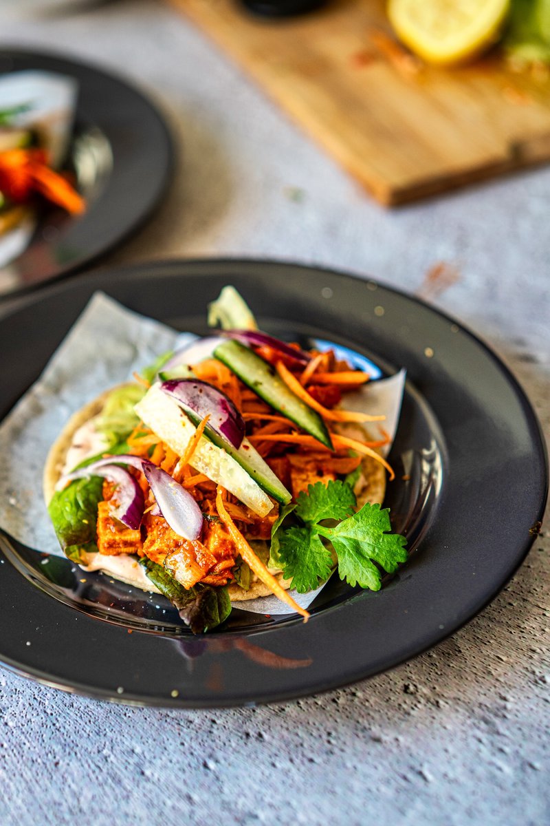 Tofu bell pepper taco topped with sliced vegetables and fresh herbs on a black plate.