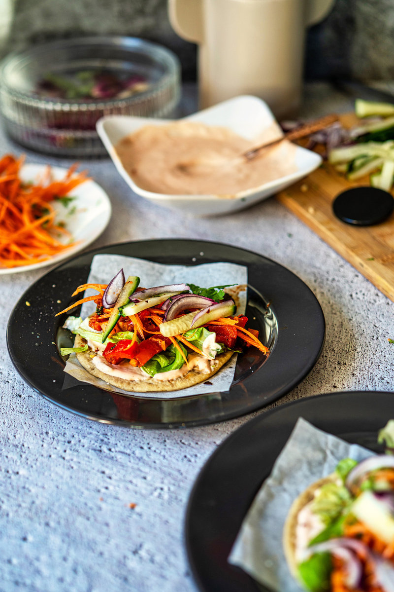 Tofu and bell pepper taco garnished with sliced onions and carrots on a black plate.