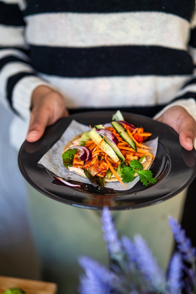 A person holding a plate with a tofu taco topped with bell peppers, onions, and cilantro.