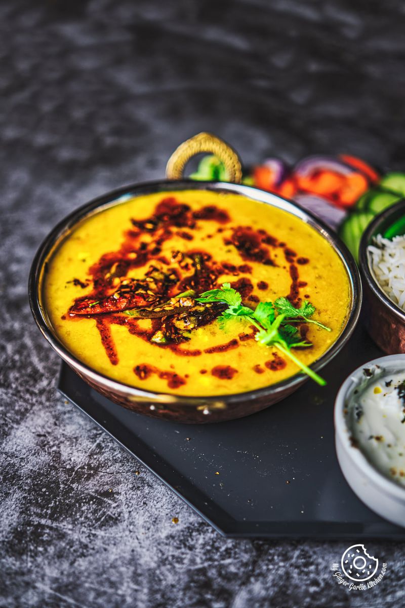 Spicy toor dal in a copper bowl, richly garnished with cilantro, showcased on a modern slate platter.