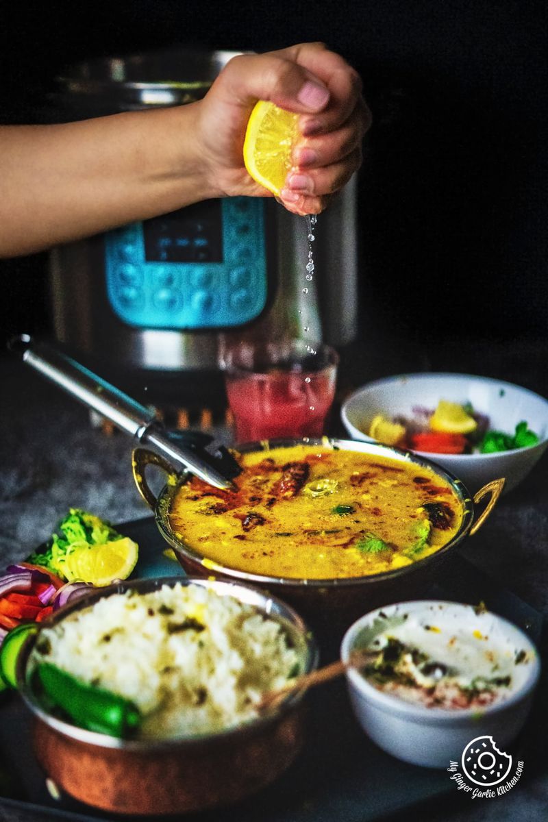a hand is adding a squeeze of lemon to a freshly prepared Toor Dal in an atmospheric kitchen setting.