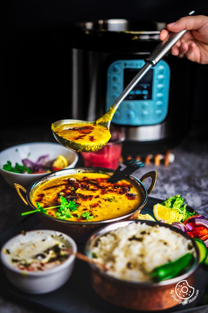 a hand is ladling aromatic Toor Dal Tadka from a copper bowl, perfectly paired with rice and condiments