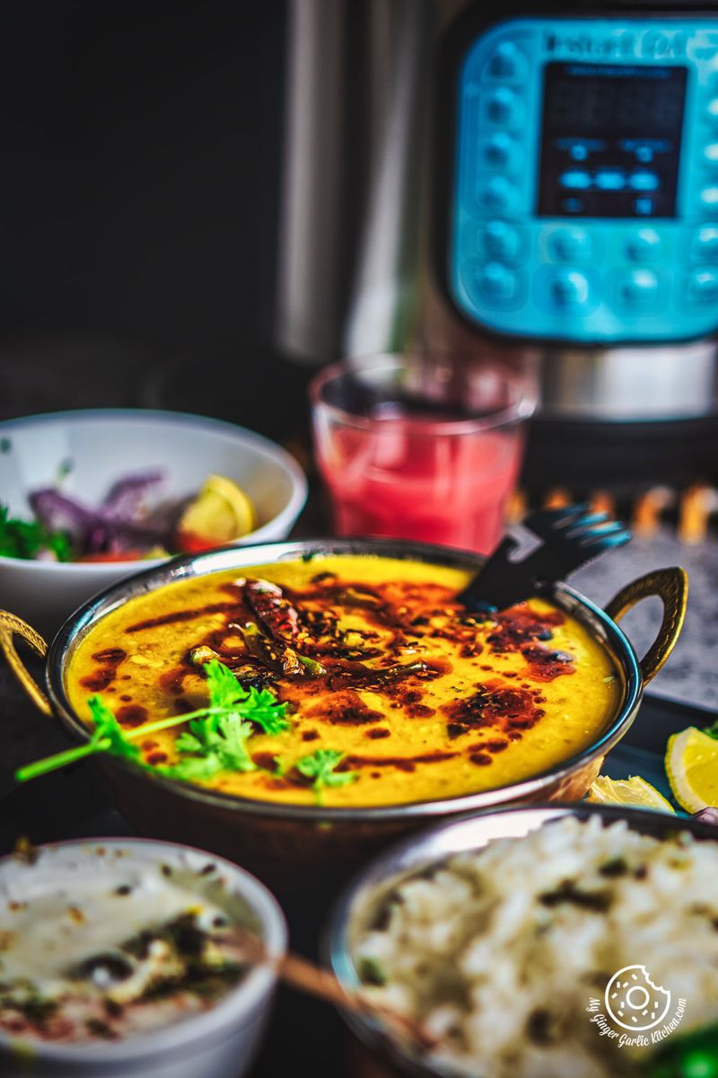 Rich and creamy Toor Dal topped with red chili tadka, accompanied by fresh slices of vegetables and rice