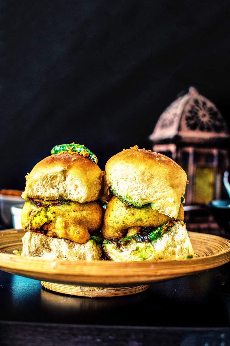 A plate of vada pav, a popular Indian street food made with a batata vada (potato patty) sandwiched between two slices of pav (bread).