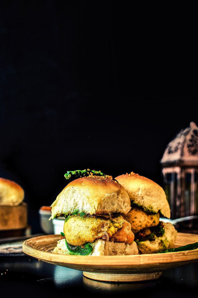 a plate with two vada pav, a popular Indian street food made with a potato patty and a bun on it, on a table