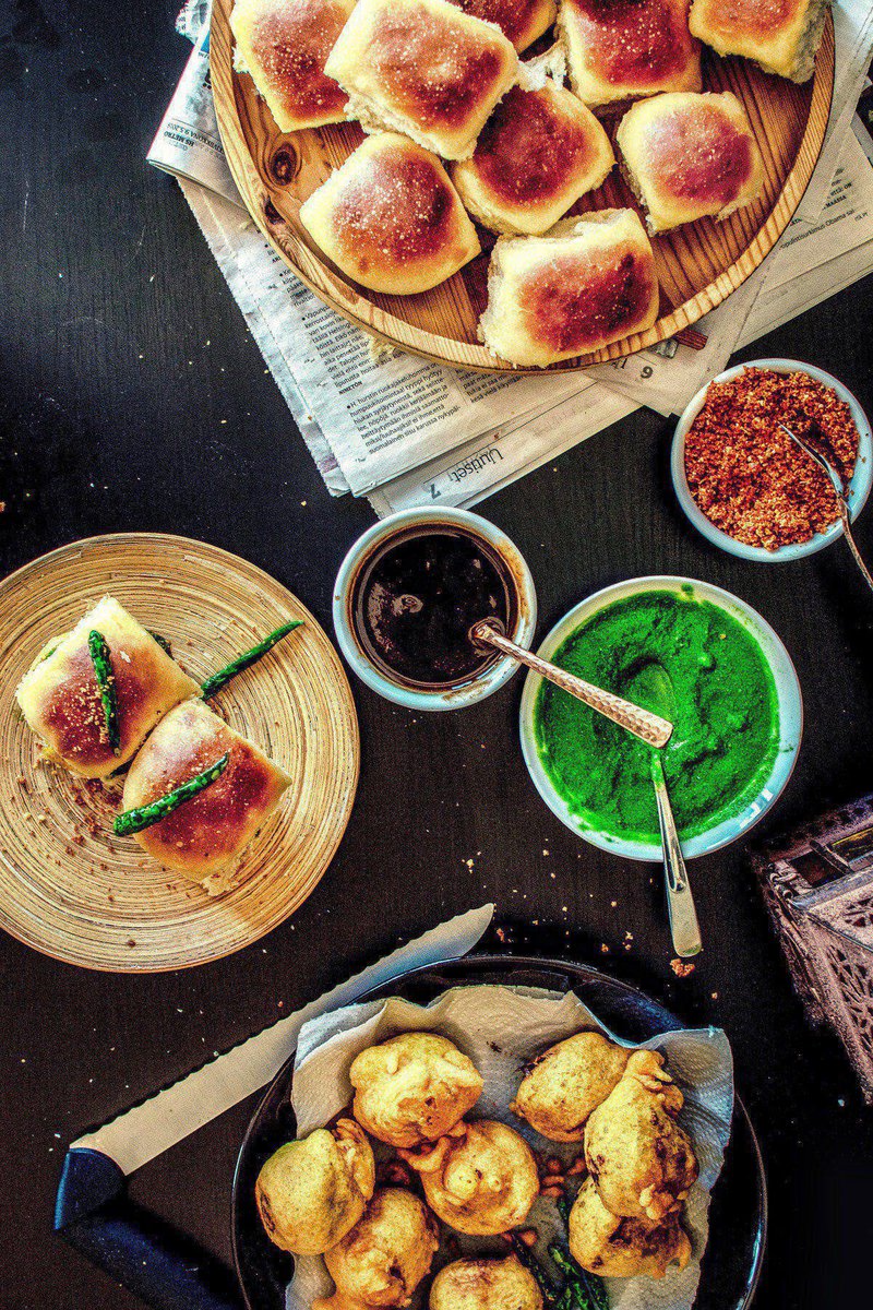 table with a plate of vada pav, a popular Indian street food made with a potato patty and a bun and bowls of chutneys