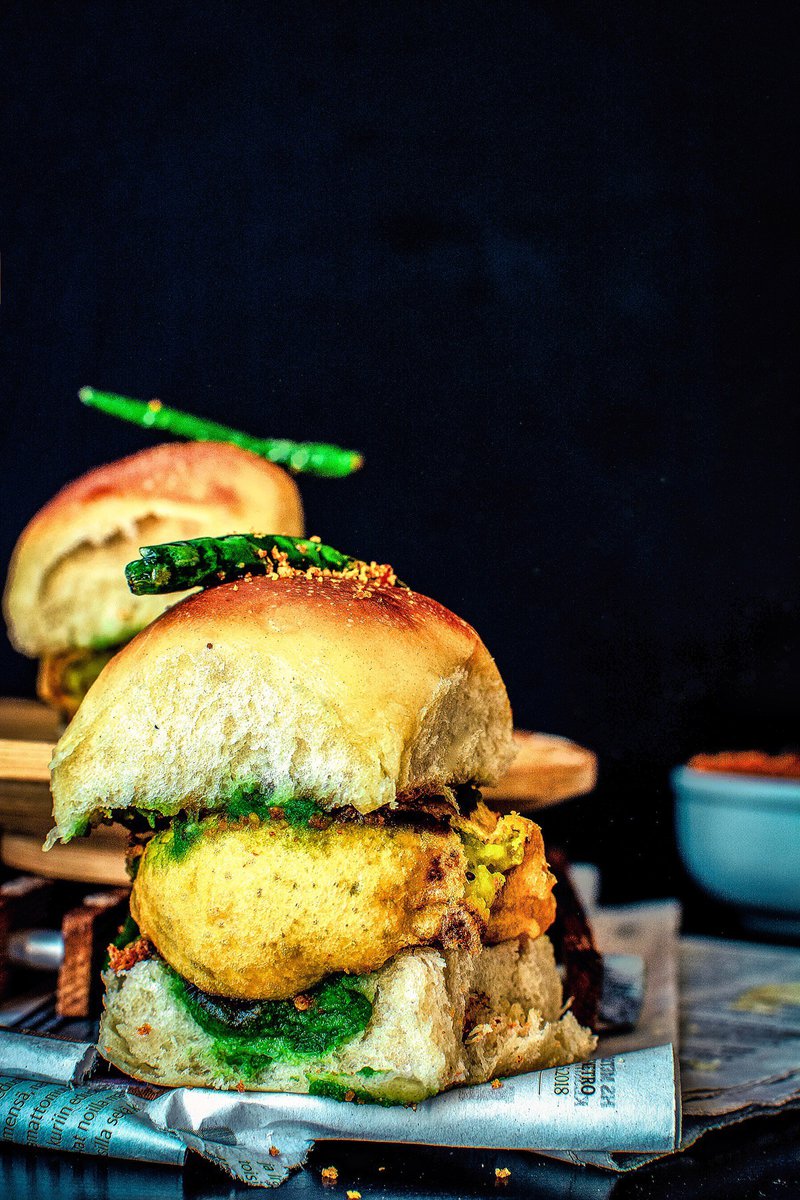 A vada pav is a popular Indian street food made from a batata vada (a potato patty) sandwiched between two slices of pav (a bread bun). It is typically served with a green chutney and a tamarind chutney.