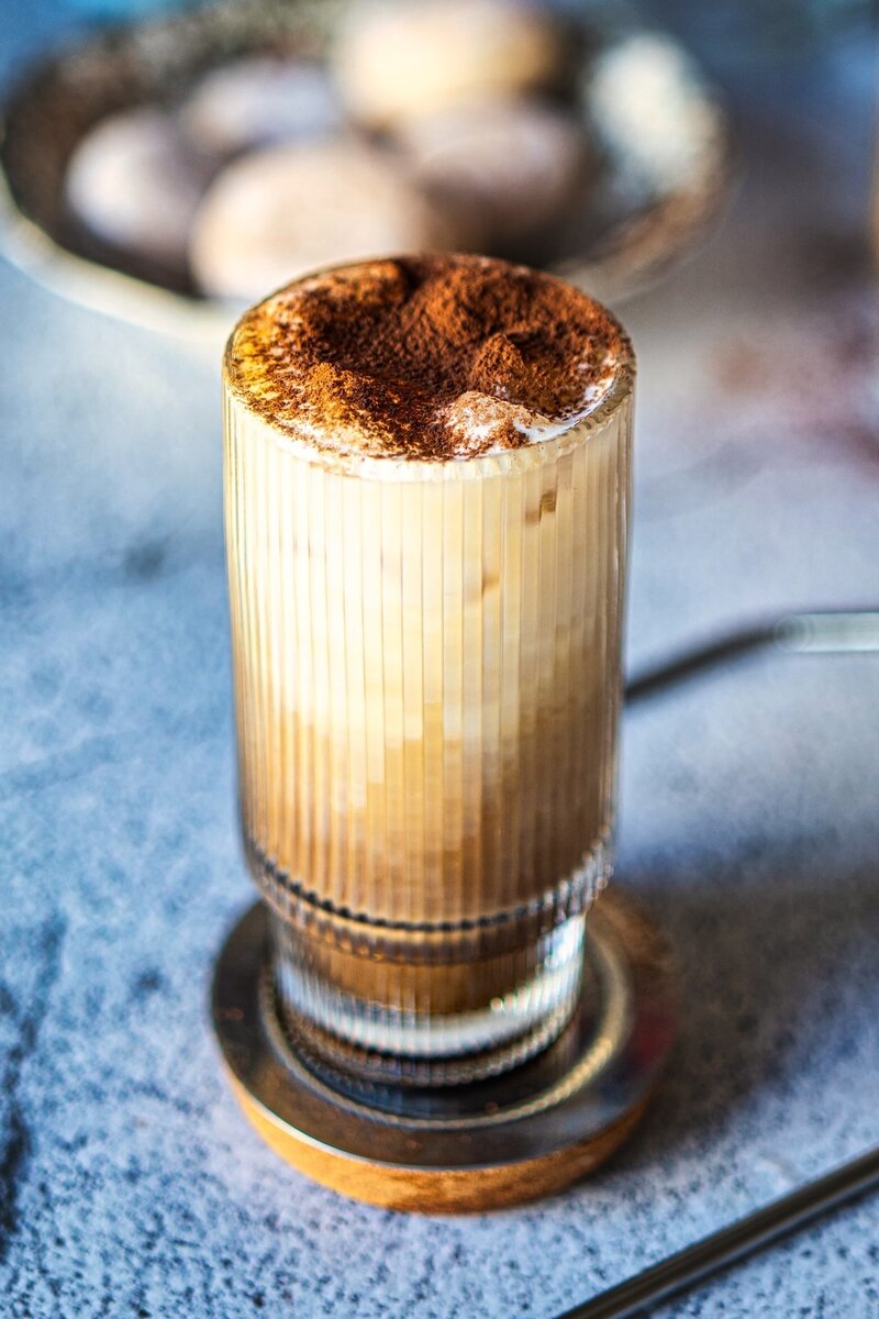 Creamy vanilla iced latte with frothy milk and cocoa powder topping in a tall glass, café-style iced coffee at home