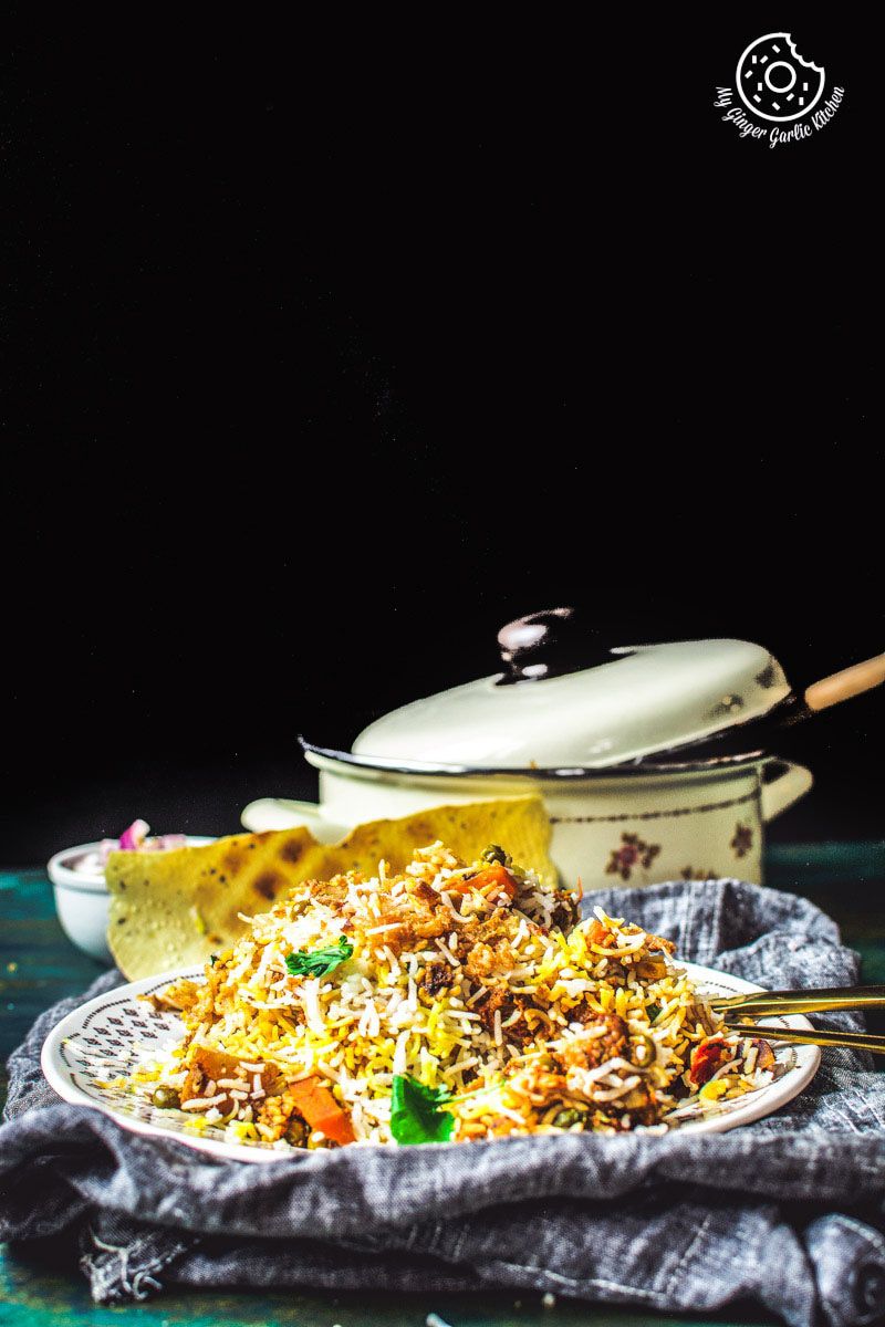 there is a plate of restaurant style hyderabadi veg dum biryani  with rice and vegetables on it
