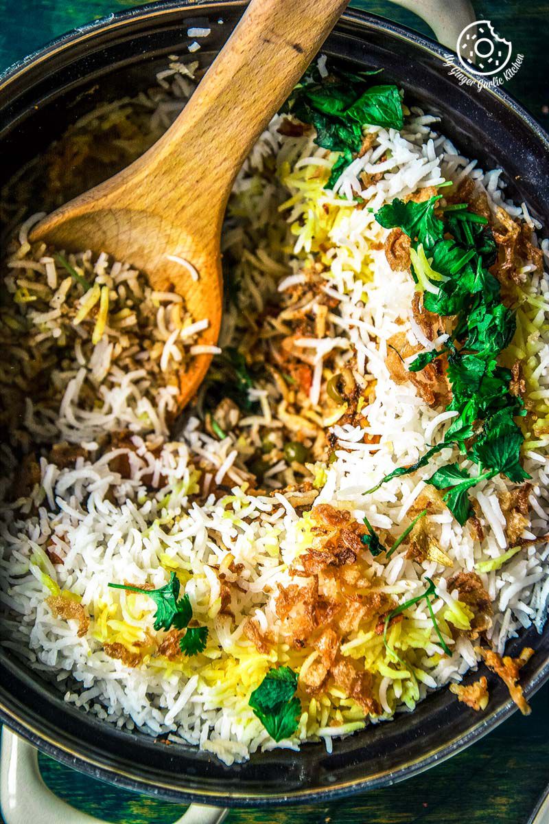 there is a pan filled with restaurant style hyderabadi veg dum biryani and a wooden spoon