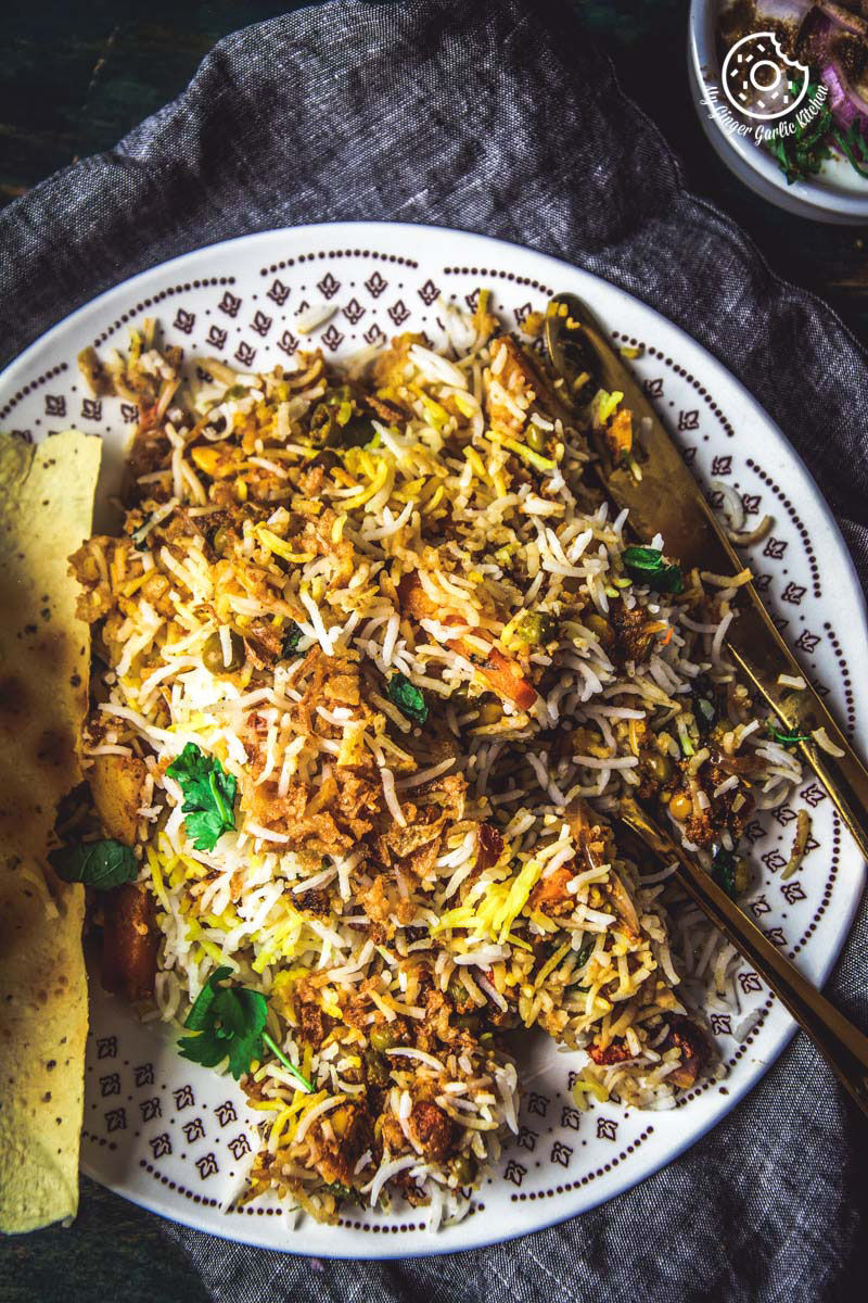 there is a plate of restaurant style hyderabadi veg dum biryani with a fork and a plate of rice