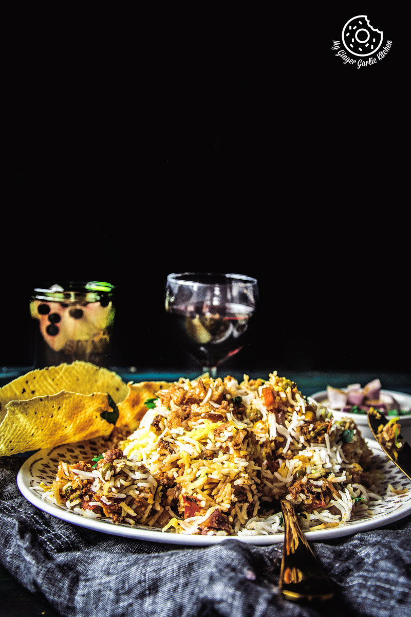 there is a plate of restaurant style hyderabadi veg dum biryani on a table with a glass of wine