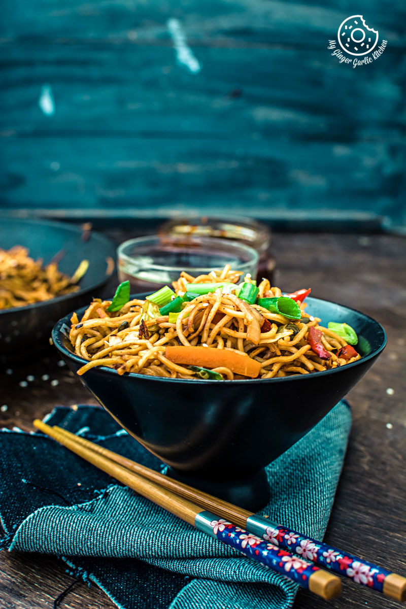 a bowl of veg schezwan noodles with chopsticks on a table